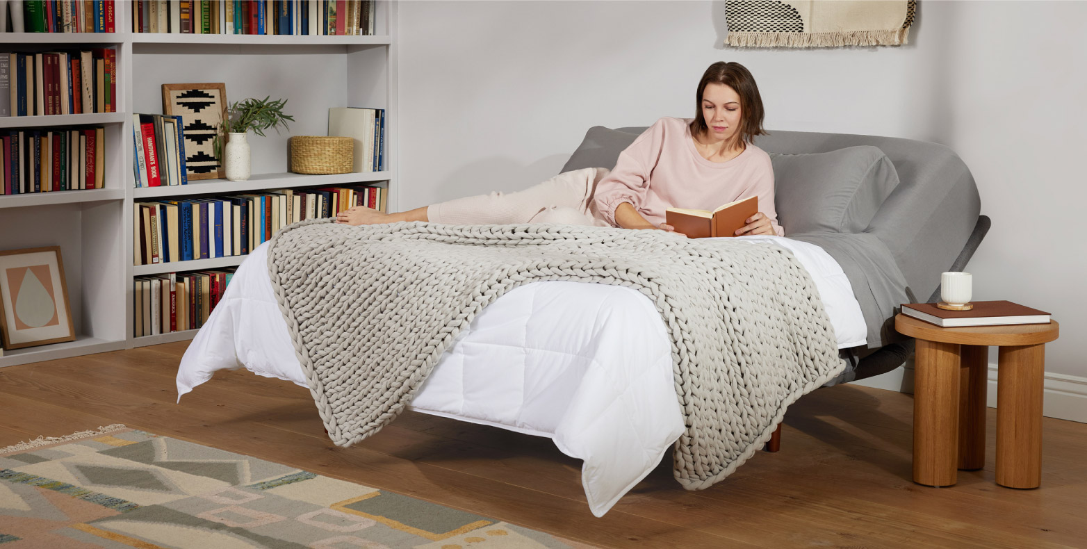 A young woman reading a book on an adjustable bed.