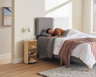 Man sleeping in a bed with a grey upholstered bed frame. 