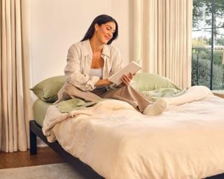 A woman reading in bed, her mattress on a Purple metal platform base.