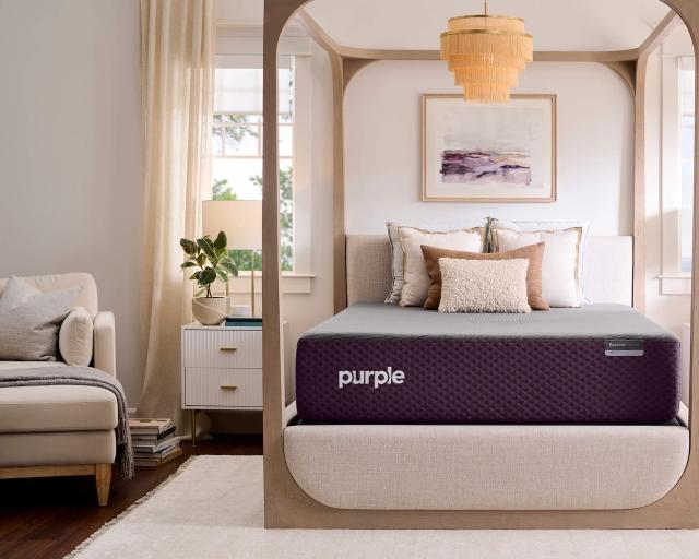 A Purple RestorePremier Hybrid mattress sits on a four poster canopy bed frame in a bedroom with ivory accents.