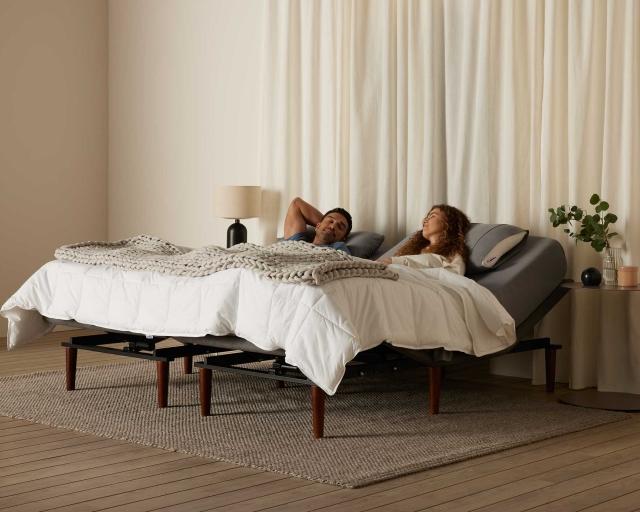 A couple sleeping together in a bed in a large room with white curtains. 