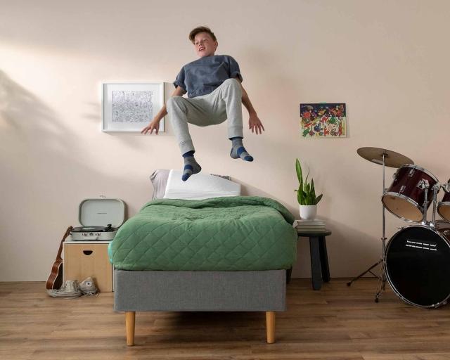 An exuberant child jumping on a twin size mattress in a bedroom.