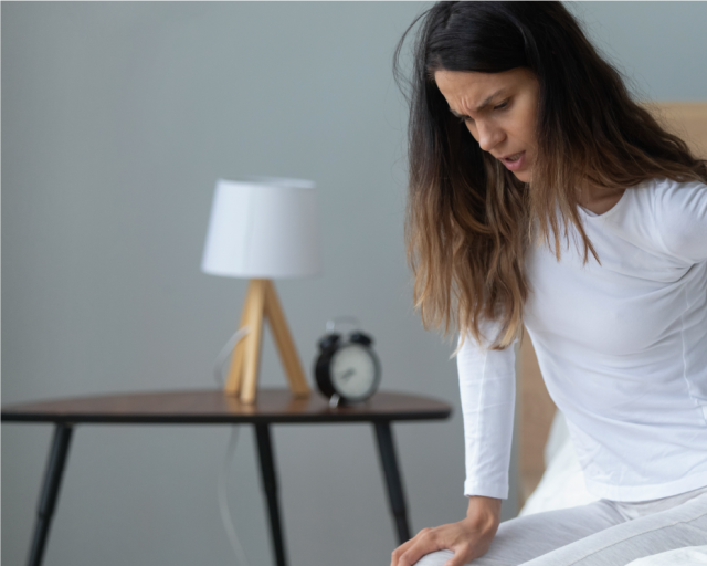 A woman rubs her lower back due to new mattress back pain.