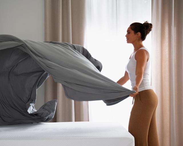 Woman placing a top sheet on a bed.