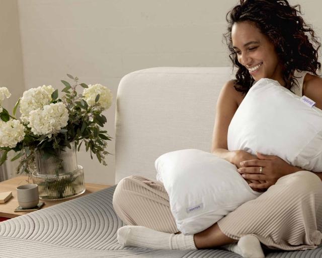 Woman holding a pillow sitting on bed.