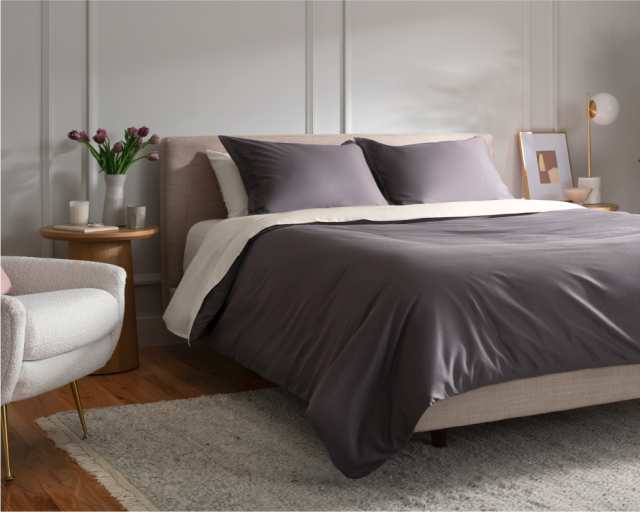 Bedroom with a made bed with grey and white sheets.