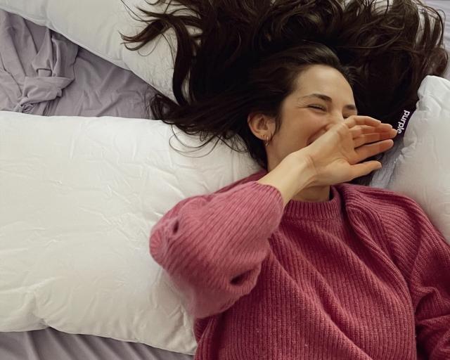 Woman lying on her back surrounded by three Purple pillows. 