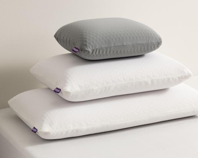 Three Purple pillows stacked on top of each other on a bed from largest to smallest 