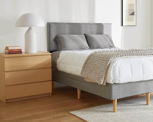 A mattress covered with a duvet and blanket on top of the Purple Bed Frame in a bright bedroom.