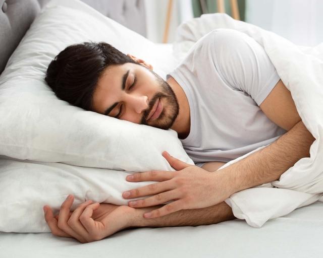 A man sleeping on his side cover with two pillows and covered in a white duvet.