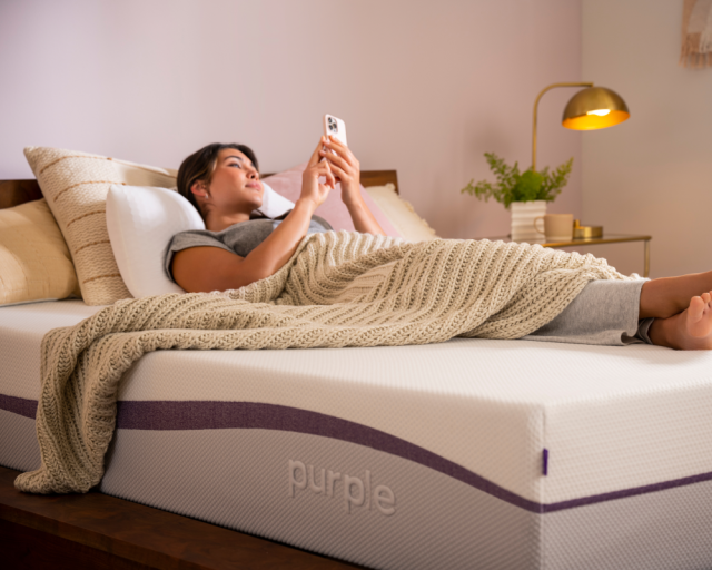 A woman scrolling on her phone while unable to sleep on a Purple Plus mattress.