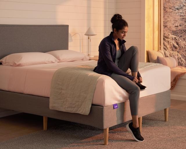 A woman sitting on a Purple mattress in warm lighting.