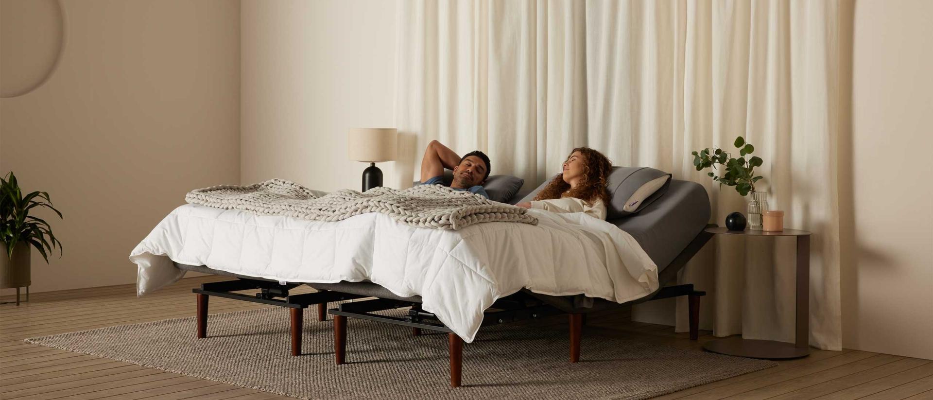 A couple sleeping together in a bed in a large room with white curtains.