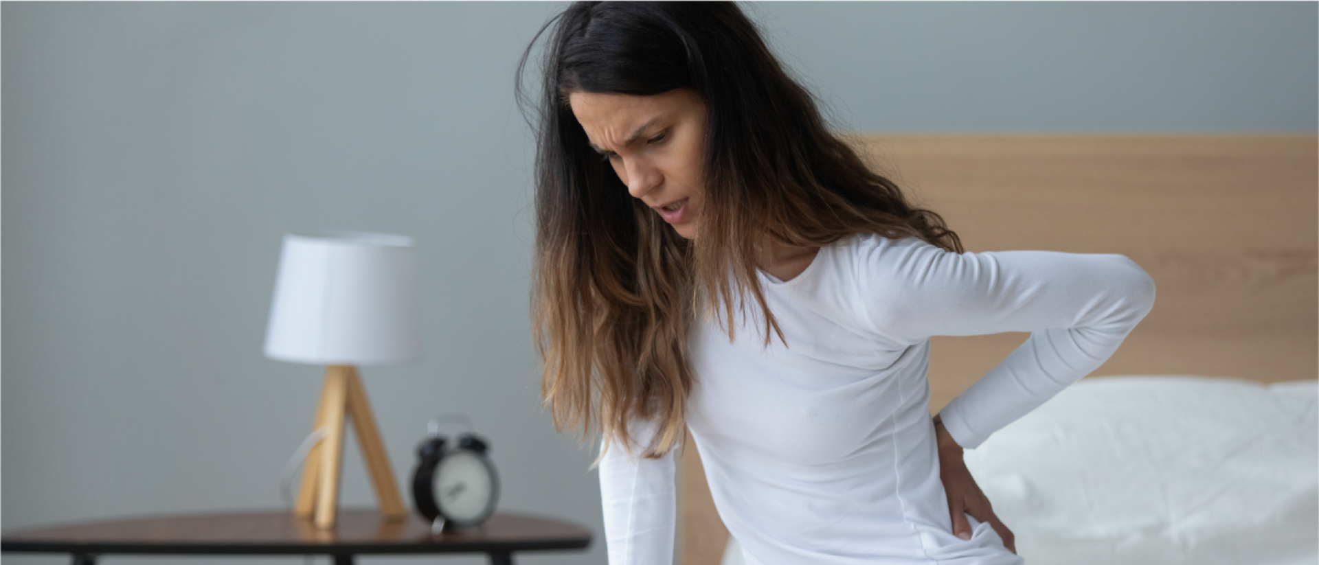 A woman rubs her lower back due to new mattress back pain.