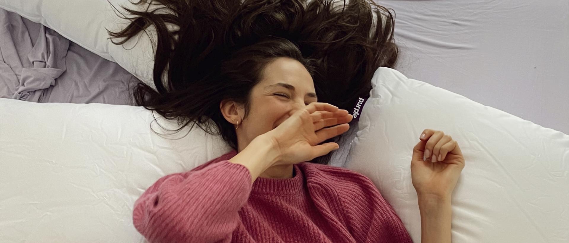 Woman lying on her back surrounded by three Purple pillows. 