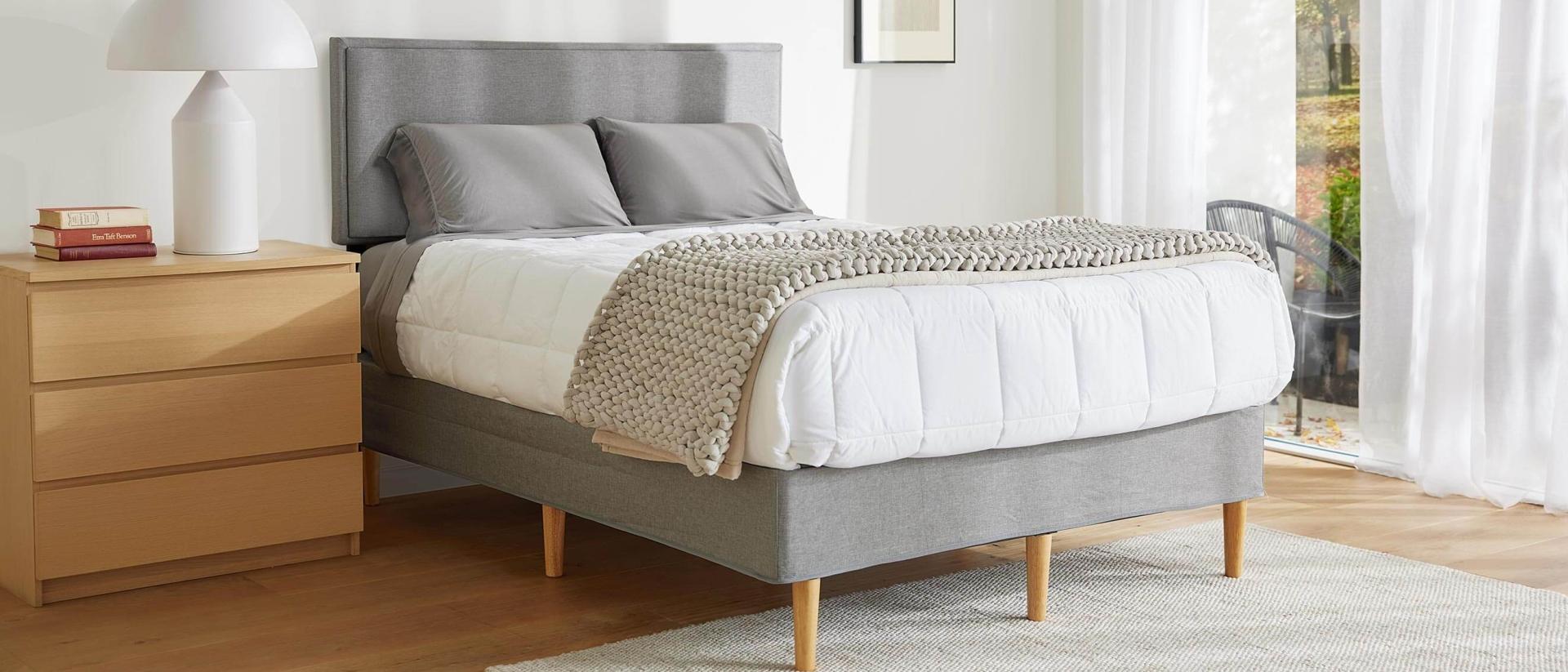 A mattress covered with a duvet and blanket on top of the Purple Bed Frame in a bright bedroom.