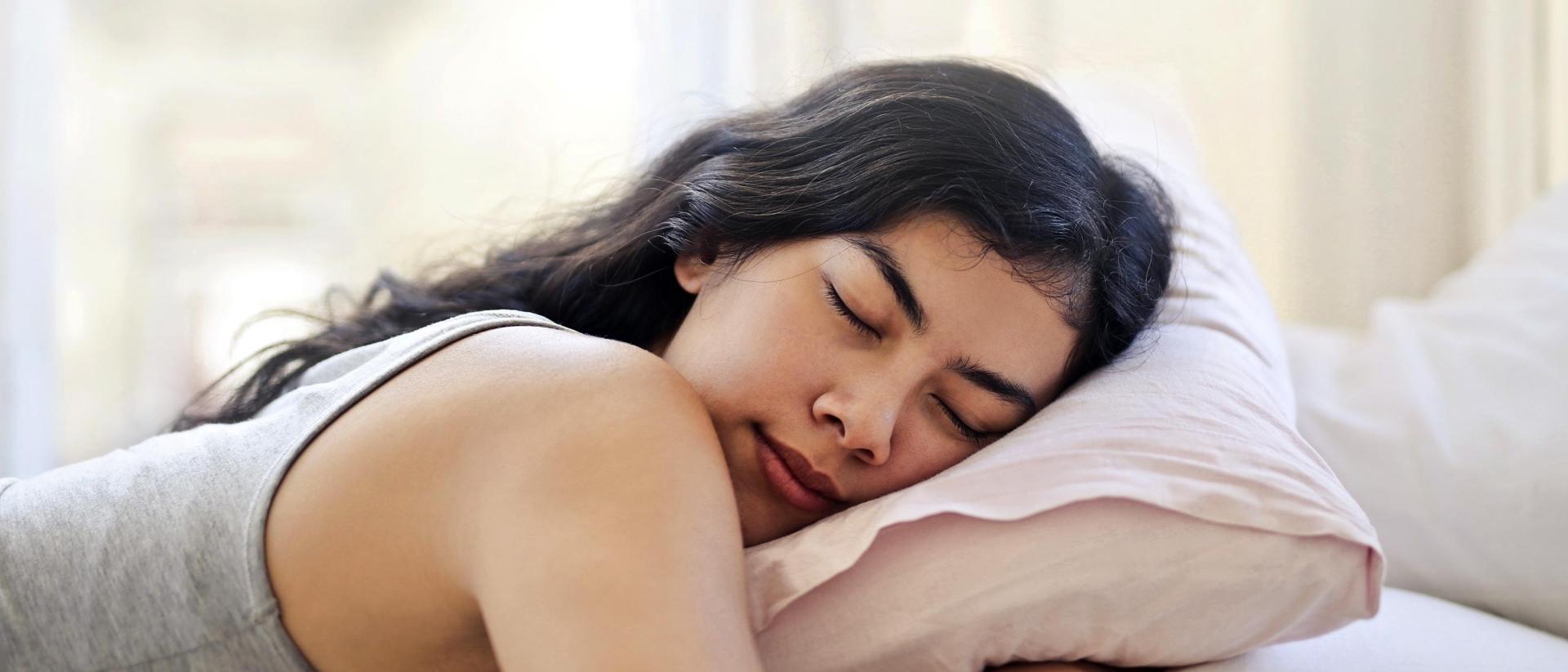 Woman sleeps on her stomach while hugging her pillow with her face turned to the side.