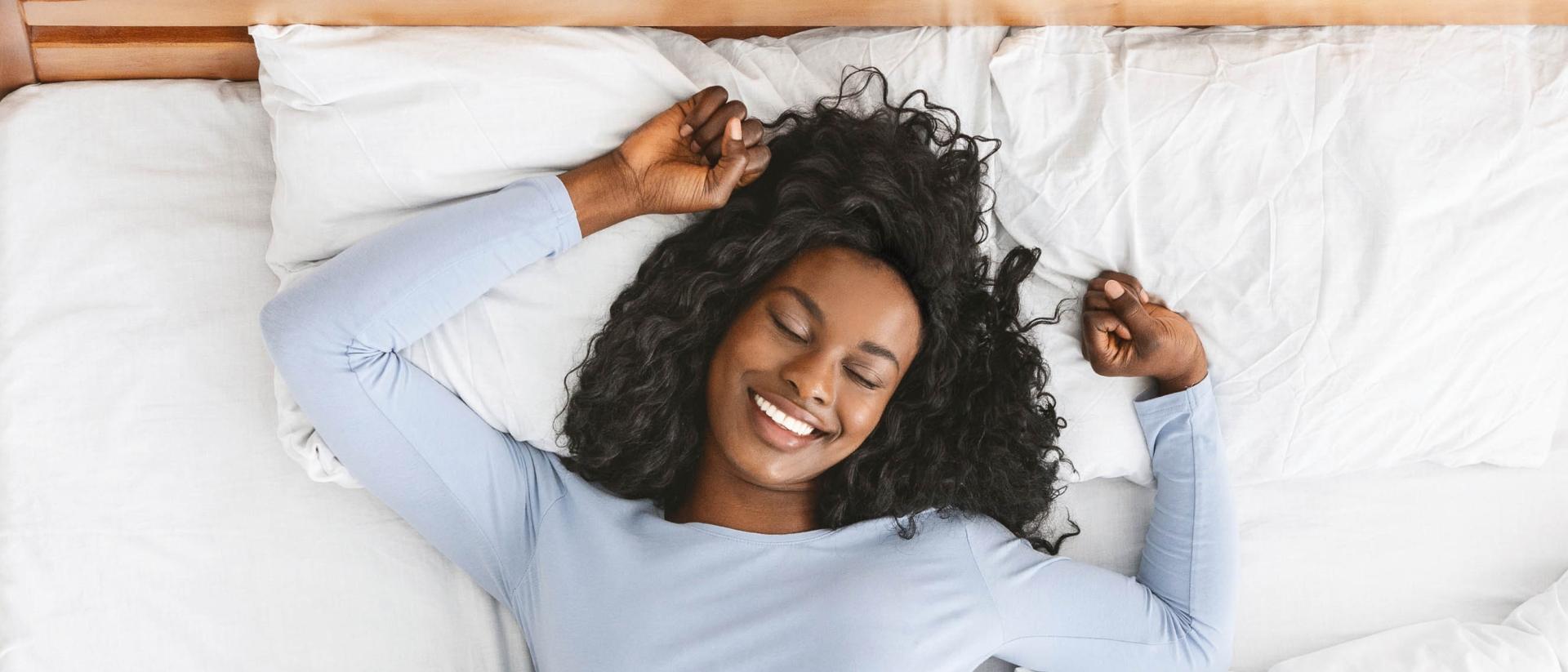 A smiling woman lying on her back in bed.