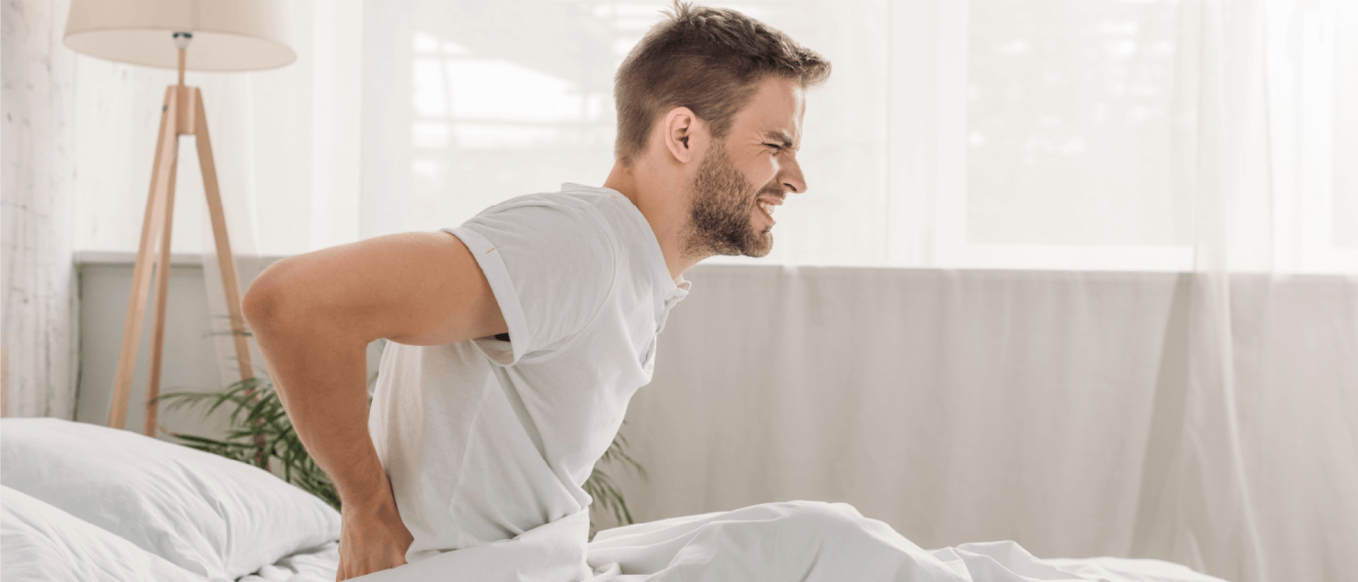 A man wakes up with a sore back after sleeping on a bad mattress.