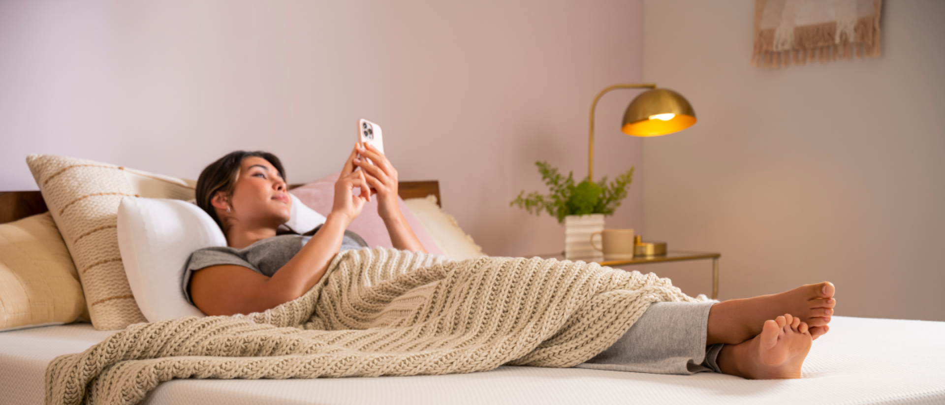 A woman scrolling on her phone while unable to sleep on a Purple Plus mattress.