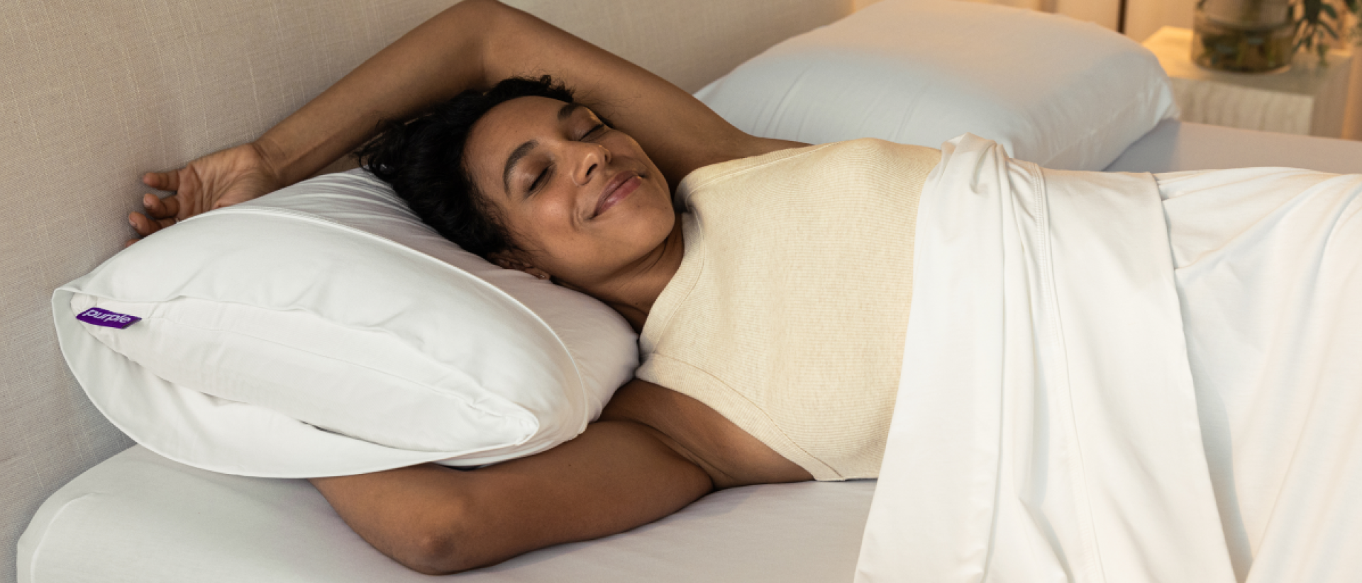 A woman stretching on a mattress and Purple Harmony pillow.