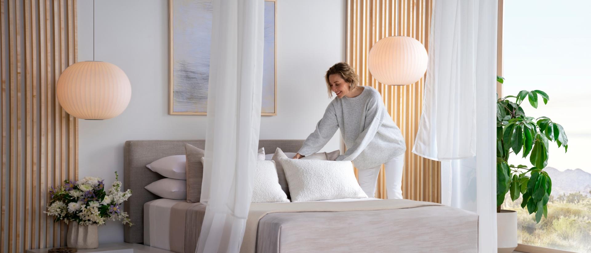 A woman making the bed with a Purple Rejuvenate mattress.